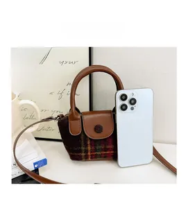 Mini borsa in tweed a quadri con tracolla marrone accanto a uno smartphone per dimensione