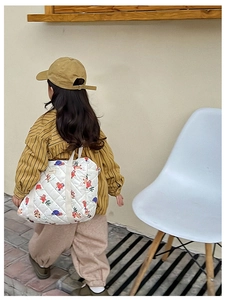 Rear view of a child wearing a quilted floral bear print crossbody bag in a modern room