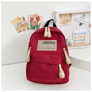 Détail du sac à dos en toile bordeaux avec étiquette de mode et tirettes de fermeture