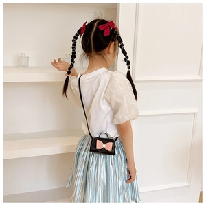 Rear view of a girl wearing a black PU leather crossbody bag with a large pink bow