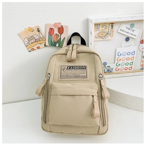 Détail d'un sac à dos enfant beige minimaliste avec étiquette FASHION et tirettes en cuir