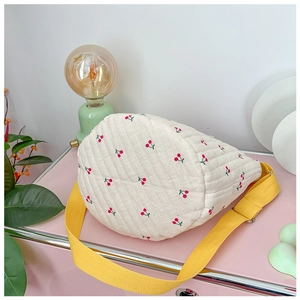 Détail du sac seau matelassé crème avec broderie cerise et bandoulière jaune