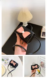 Detail of mini black textured leather crossbody bag featuring a pink bow and shoulder strap