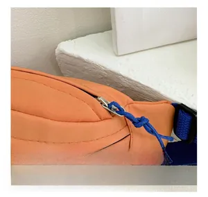 Detail view of durable metal zipper and stitching on the vibrant orange nylon belt bag