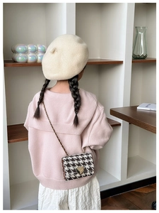 Detail of child wearing a plaid crossbody bag with a gold heart clasp and chain strap