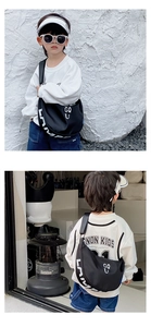 Detailed view of child wearing black nylon crescent bag with white GQ U letter print