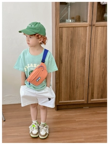 Close-up of vibrant orange canvas kids chest bag with letter logo patch on street style model
