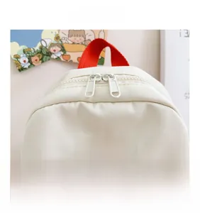 Top detail view of canvas backpack with red handle and dual metal zippers