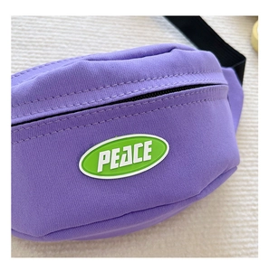 Detail of purple canvas fanny pack featuring a green PEACE patch and black zipper strap