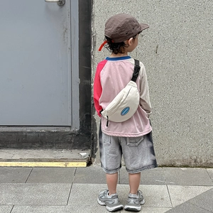 Child wearing white canvas crossbody chest bag with blue label, outdoor casual style