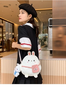 Detail view of a cute rabbit-shaped canvas crossbody bag with pink ears and plush pendant