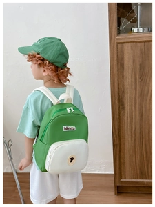 Kid modeling a contrast green and beige canvas backpack with adjustable straps and letter patch
