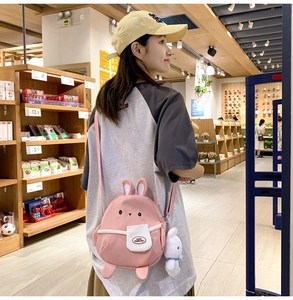 Detail of pink cartoon rabbit crossbody bag showing embroidery and plush pendant charm