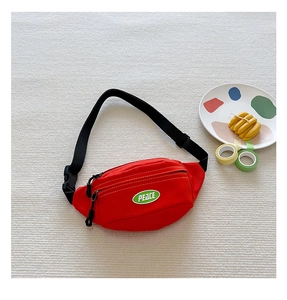Detail of red canvas kids sling bag featuring a green PEACE patch and adjustable strap