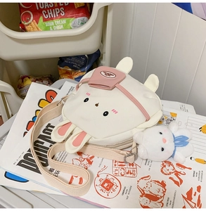 Detail of cute rabbit canvas crossbody bag with plush charm on magazines in a cozy home setting