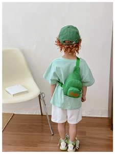 Green canvas kids crossbody bag with orange text detail shown in a casual lifestyle setting