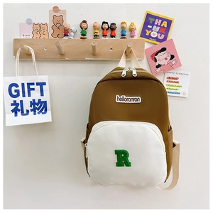 Close-up of canvas backpack featuring a green letter R patch and brand woven label