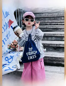 Outdoor shot of a blue denim drawstring backpack for kids with white cotton rope straps