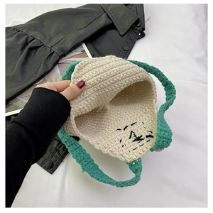 Close-up of handmade crochet bag in cream and green with knitted cartoon face detail