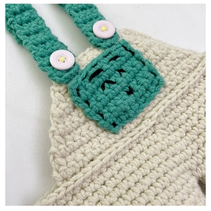 Detail of crochet baby overall with green straps, pink buttons and star stitching