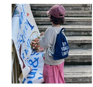 Rear view of child wearing a blue canvas drawstring backpack with white lettering detail