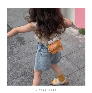 Fillette portant un sac bandoulière orange avec nœud blanc et chaîne dorée dehors