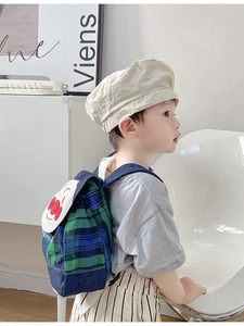 Detail of plaid kids backpack with cartoon face flap and matching beige cotton newsboy hat