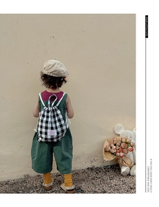 Rear view of child wearing vintage green overalls with a black and white checkered backpack