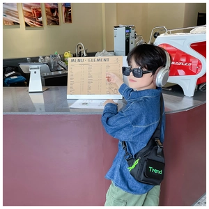 Detail showing kids black nylon crossbody bag with green Trend text in a cafe setting