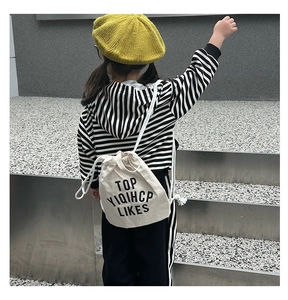 Close-up of child carrying a white canvas drawstring bucket bag with black letter print