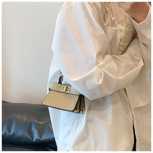 Dettaglio mini borsa in pelle beige con chiusura rotante dorata e manico superiore