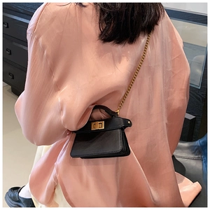 Dettaglio mini borsa a tracolla nera con catena dorata su una camicia di raso rosa
