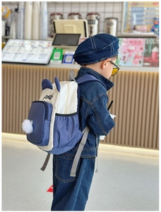 Detail eines Kinderrucksacks im Farbblock-Design mit Panda-Ohren und Plüschball-Anhänger