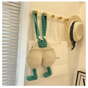 Detail of creative handmade crochet crossbody bag with green overalls design on hook