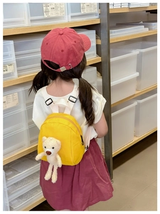 Detail of cute teddy bear plush attached to a bright yellow canvas mini backpack for kids