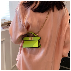Mini borsa a tracolla verde neon con catena dorata e manico su sfondo camicia rosa