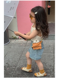 Détail d'un mini sac bandoulière orange avec bords ondulés et chaîne dorée sur enfant