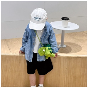 Kid modeling a green handmade crochet dinosaur crossbody bag with casual outfit