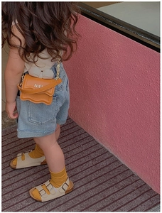 Détail du sac orange pour fille avec nœud blanc, bords ondulés et chaîne dorée