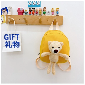 Detail of a bright yellow canvas mini backpack featuring a plush brown 3D bear doll