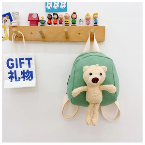Detail of light green canvas mini backpack with a plush bear toy on a wooden hook