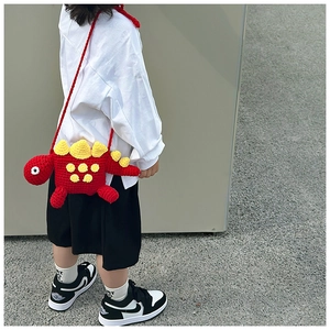 Kid's red crochet dinosaur crossbody bag shown on a young model in a street style setting
