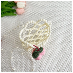 Detail of handmade beaded pearl crossbody bag with crochet strawberry charm for girls