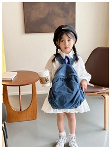 Detailed view of kids denim backpack with zippered front pocket on a child model