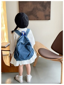 Detail of a child's blue denim backpack featuring durable fabric handles and vintage style