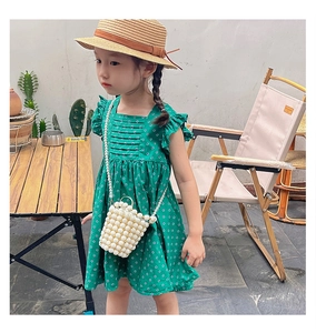 Detail of a green polka dot dress with ruffles, a straw hat, and a pearl beaded bag