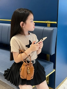 Side view of child model holding a mini caramel litchi leather bucket bag with metal buckle