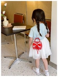 Détail du sac rouge en tweed pour fille avec poignée en perles et nœud dans un café