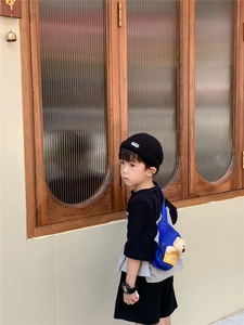 Detail of children's blue chest bag with plush bear ornament and black knit beanie hat