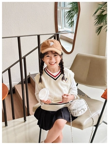 Girl in preppy knit vest and pleated skirt with quilted chain crossbody bag